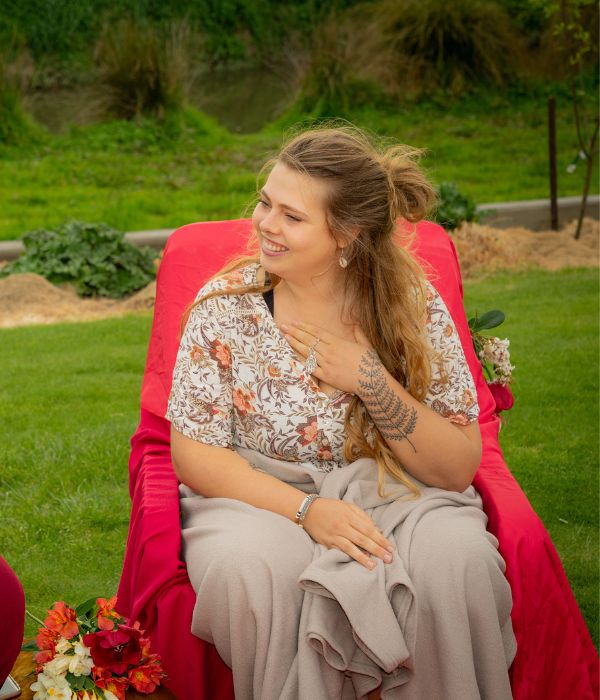 A lady outdoors sitting in a red chair with flowers.