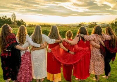 A group of eight women linking arms with their back to the camera watching the sunset.